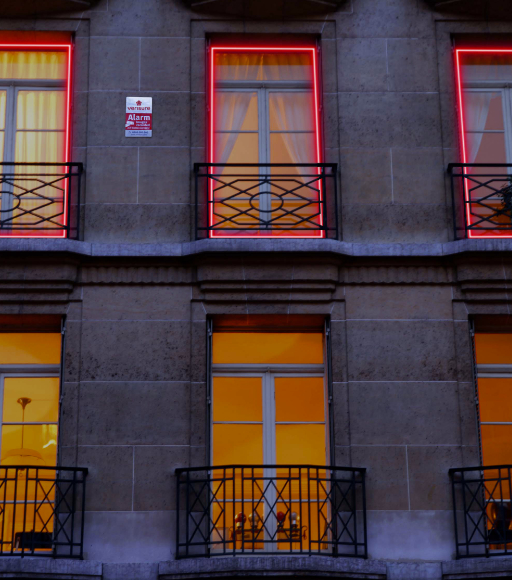 A building facade with a Verisure sign and six windows, three of which are outlined in red neon lights.