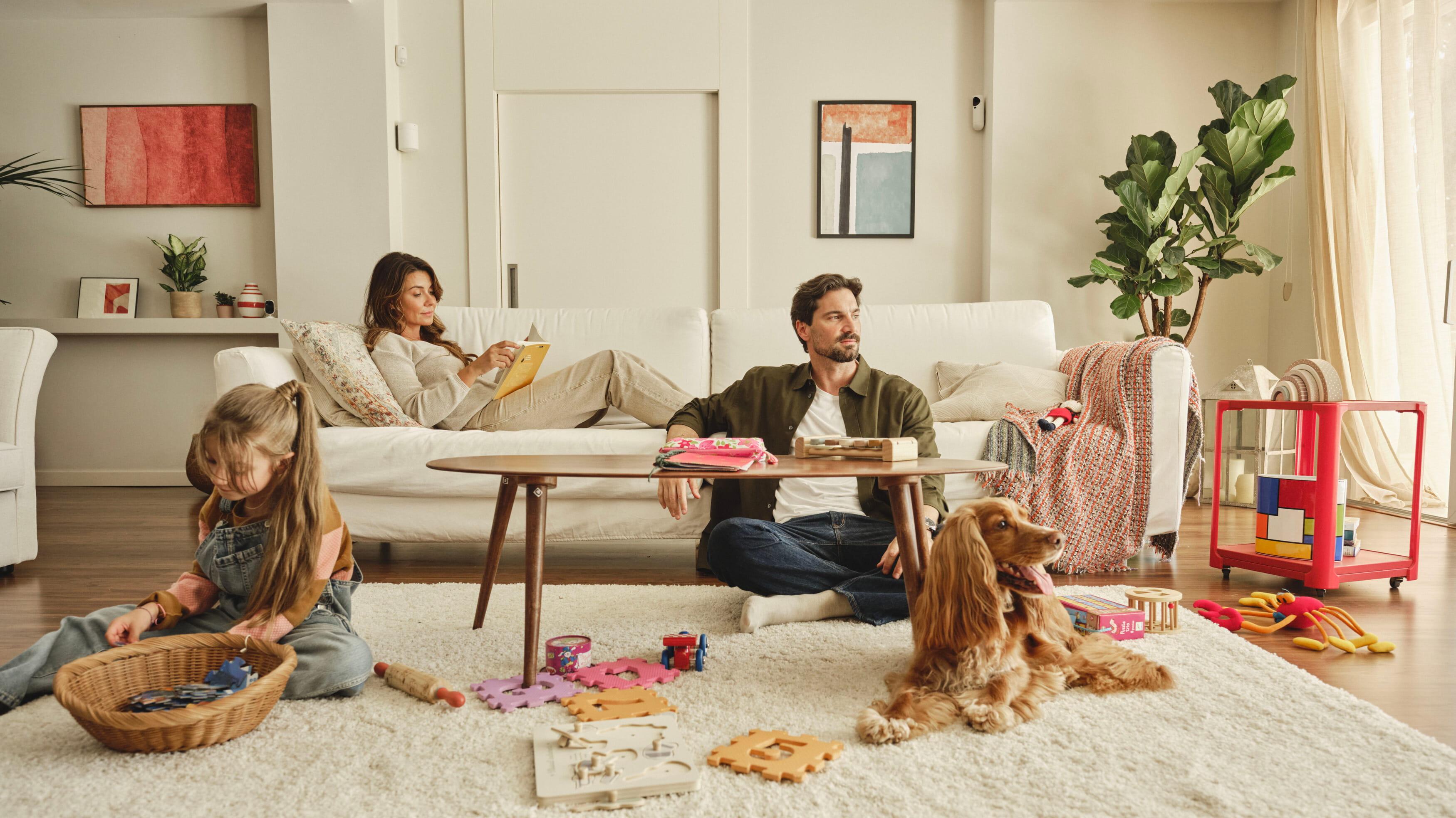 Family at home relaxing, with child playing and dog lying on floor.